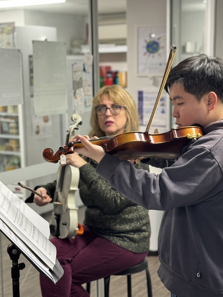 A musician practising violin with guidance from a teacher